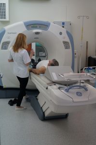 pracownik tk ubrany w ubranie ochronne medyczne koloru białego wykonuje badanie tomografem pacjentowi w pracowni TK