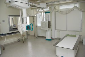 pracownia rtg wraz z aparatem do badaniań koloru białego i białym stołem do diagnostyki RTG oraz drzwiami koloru białego