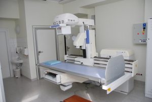 pracownia rtg wraz z aparatem do badaniań koloru białego i niebieskim łóżkiem do diagnostyki RTG oraz drzwiami koloru białego
