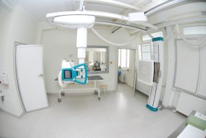 pracownia rtg wraz z aparatem do badaniań koloru białego i szarym łóżkiem do diagnostyki RTG oraz drzwiami koloru białego