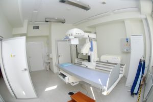 pracownia rtg wraz z aparatem do badaniań koloru białego i niebieskim łóżkiem do diagnostyki RTG oraz drzwiami koloru białego
