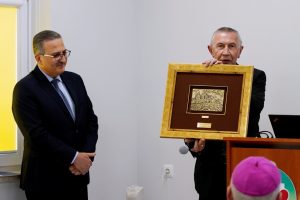 osoba ubrana w garnitur koloru czarnego wręcza pamiątkę Dyrektorowi Szpitala ubranego w garnitur koloru czarnego podczas otwarcia ZOL szpitala.