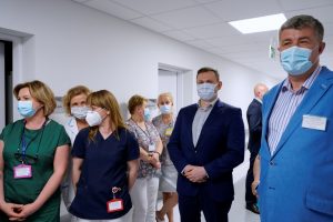 osoby ubrane w ubrania medyczne i wizytowe oraz maseczki ochronne na twarzy na korytarzu koloru białego oddziału ZOL szpitala.