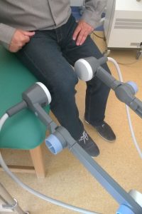 osoba ubrana w czarne spodnie i czarne obuwie podczas zabiegu rehabilitacyjnego na łóżku medycznym zielonym