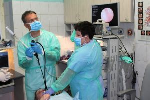 lekarz wykonujący badaniie gastroskopii wraz z pielęgniarka pacjentowi szpitala w niebieskim ubraniu ochronnym z maseczkami na twarzy