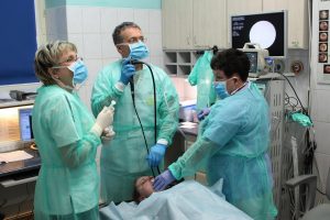 lekarz wykonujący badaniie pacjentowi szpitala w zielonym ubraniu ochronnym gastroskopii wraz z pielęgniarka w niebieskim ubraniu ochronnym i lateksowymi niebieskimi rękawiczkami medycznymi