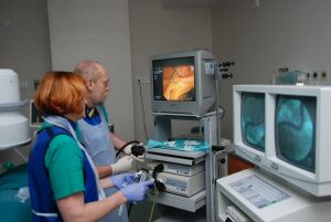 dwie osoby w ubranich koloru niebieskiego podczas operacji ogląda wykonywaną operację na trzech monitorach aparatu endoskopowego koloru białego