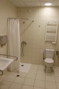 łazienka koloru białego w której znajduję się umywalka z baterią koloru białego wraz z podajnikiem papieru w kolorze srebnym z prysznicem z białym parawanem oraz kompakt WC koloru białego