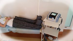 osoba leżąca na łóżku medycznym koloru niebieskiego podczas badania aparatem limfatycznym koloru biało niebieskiego na wózku medycznym obrotowym