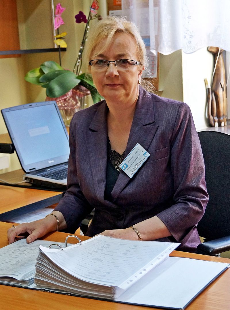 naczelna pielęgniarka w biurze przy biurku koloru brązowego z dokumentacją oraz laptopem