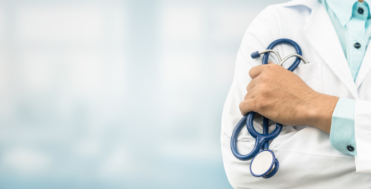 sylwetka człowieka ubrana w białe ubranie ochronne medyczne trzymająca w ręku stetyskop koloru niebieskiego