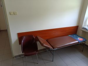 pomieszczenie poradni chirurgicznej wraz z leżakiem medycznym i krzesłem koloru brążowego