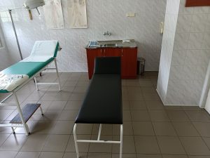 pomieszczenie poradni chirurgicznej w którym znjaduję sie dwie leżanki medyczne koloru czarengo i zielonego wraz z umywalką do mysia rąk koloru brązowego