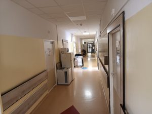 korytarz oddziału szpitala koloru białego na którym znajduje sprzęt agd koloru białego z automatycznyna dezynfekcja rąk na ścianie koloru białego