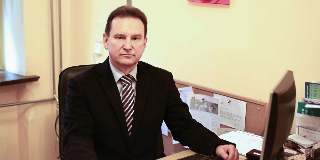 lekarz ubrany w garnitur koloru czarnego w gabinecie lekarskim koloru żółtego przy stanowiksu komputerowym