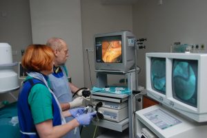 dwie osoby w ubranich koloru niebieskiego podczas operacji ogląda wykonywaną operację na trzech monitorach aparatu endoskopowego