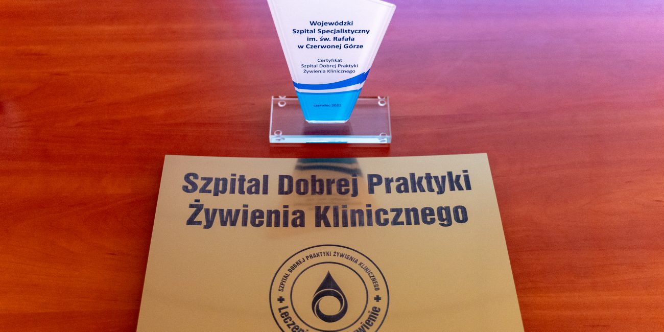 na tle brązowym znajduję sie certyfikat dla szpitala koloru białego z niebieska anotacją Szpital Dobrej Praktyki Żywienia Klinicznego