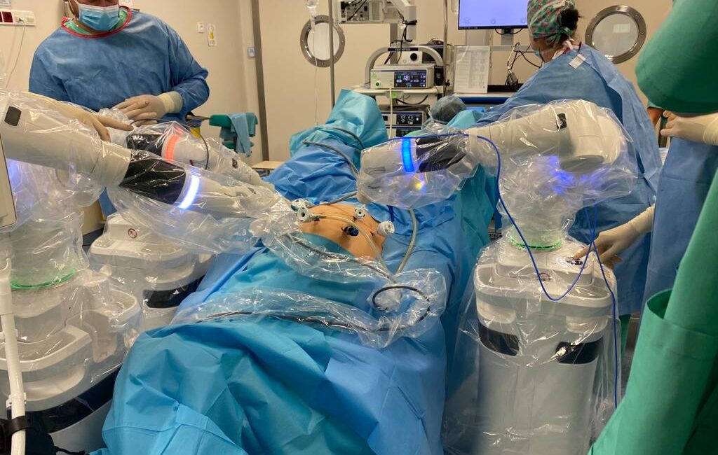 Fotografia przedstawia sale operacyjną, personel i urządzenia medyczne. Personel podczas wykonywania zdjęcia przeprowadza operacje