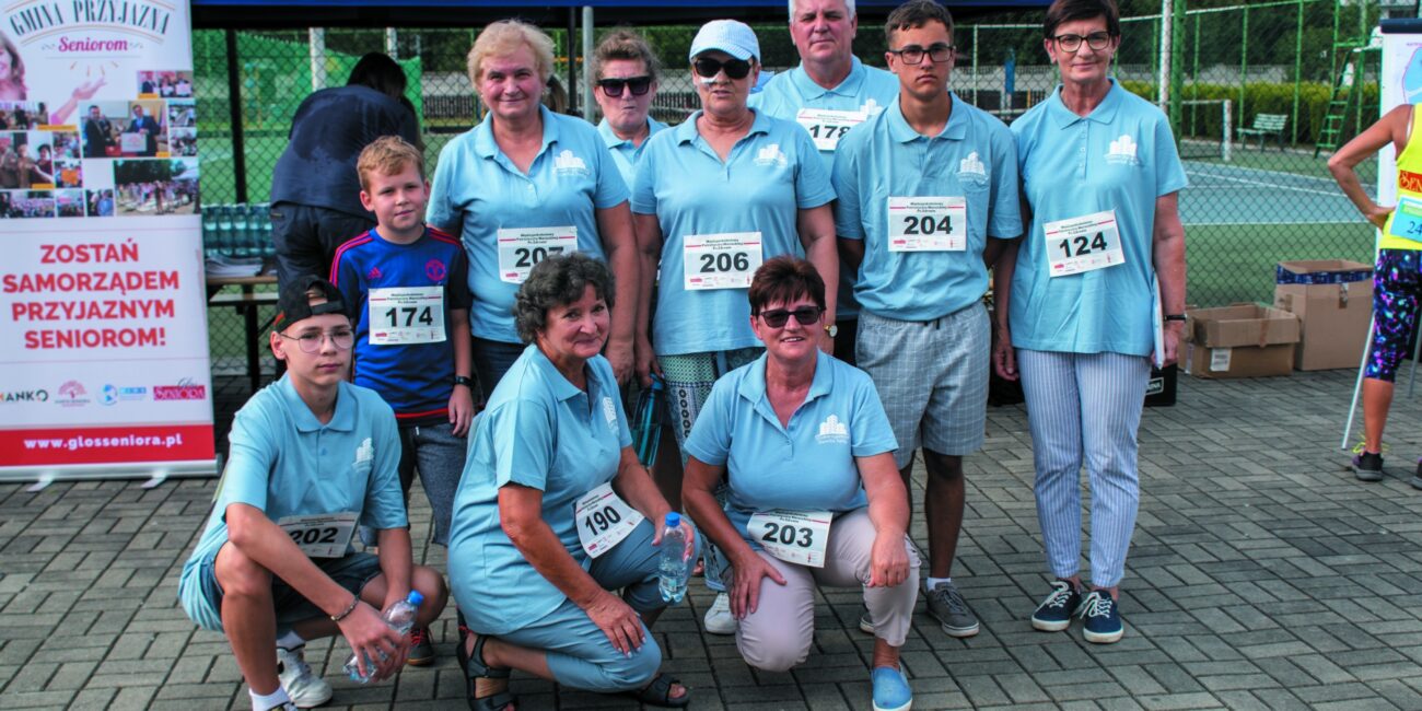 Grupa osób pozująca do zdjęcia, z naklejonymi numerami startowymi.