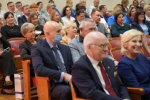 Fotografia przedstawia grupę osób siedzących i słuchających przemówienia