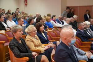 Fotografia przedstawia grupę osób siedzących i słuchających przemówienia