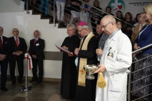 Biskup, wraz z tłumem osób na szpitalnym korytarzu