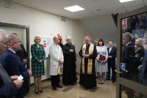 Grupa osób, stojąca na szpitalnym korytarzu w towarzystwie biskupa kieleckiego