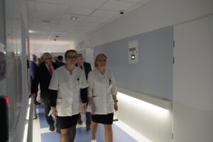 Grupa osób, Pań i Panów spacerująca po szpitalnym korytarzu